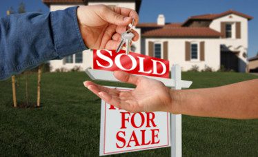 People closing the sale in front of a house and for sale sign.